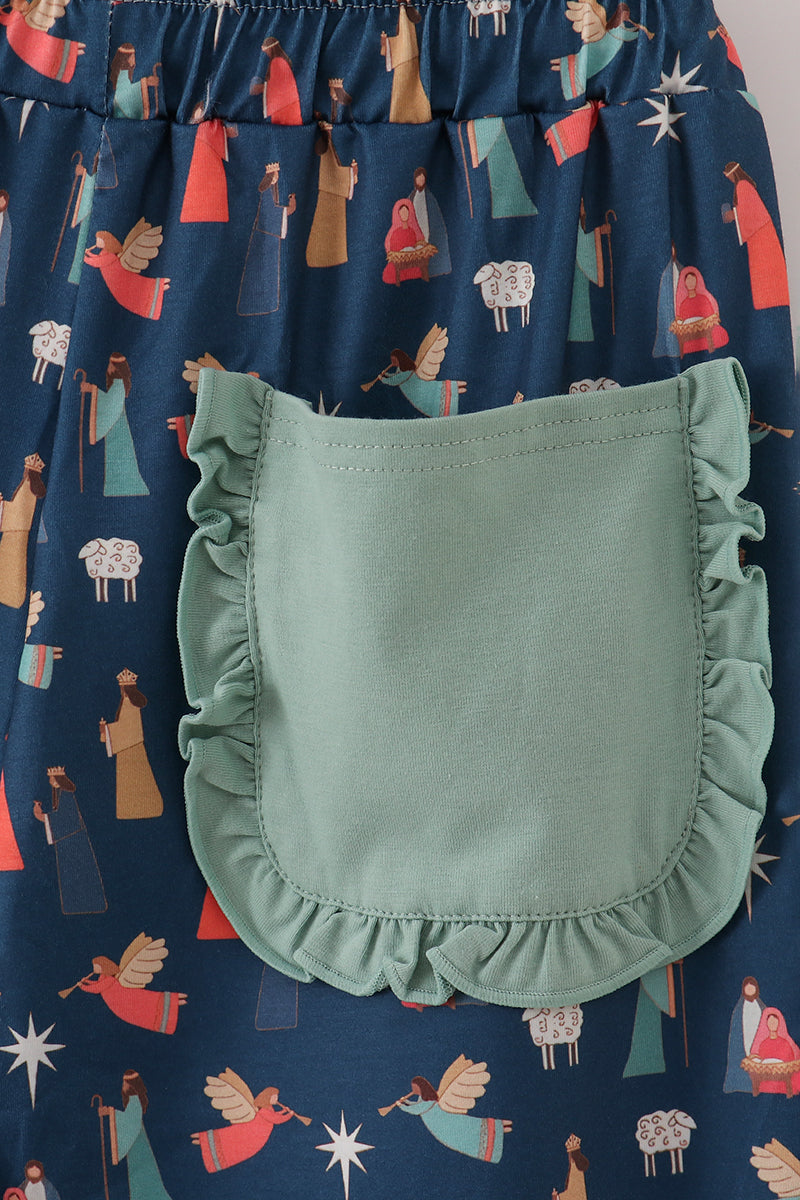 Close-up of the ruffle-trimmed mint-green patch pocket on navy Nativity-print pajama pants