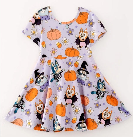 Front of lavender girls dress with cartoon dogs in Halloween costumes, orange pumpkins, candy corn, and flowers.