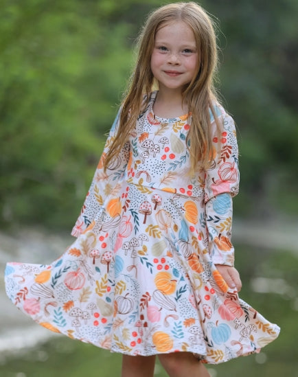 Child modeling the fall pumpkin leaf print dress outdoors.