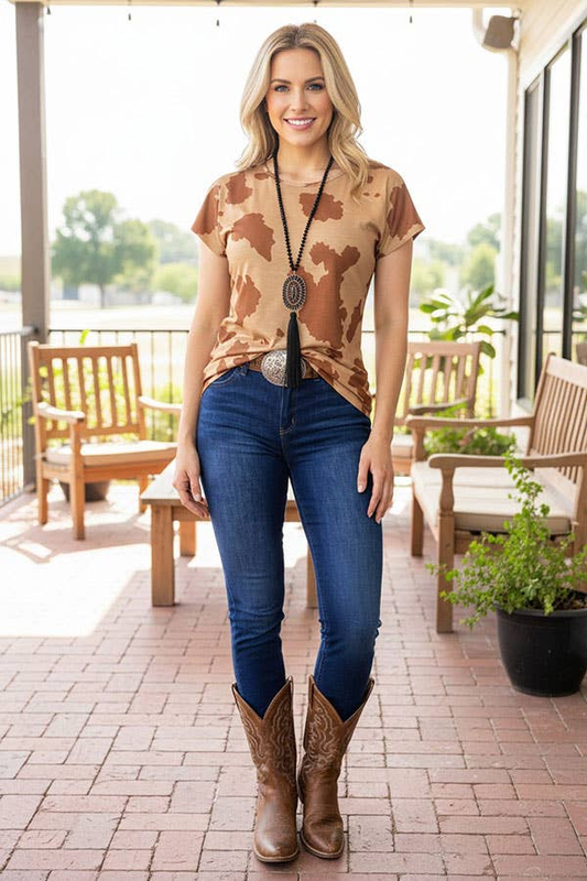 Woman wearing a tan and brown spotted short-sleeve Western top with jeans and boots.
