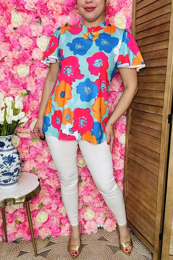 Woman wearing colorful floral lace-trim top with white trousers.